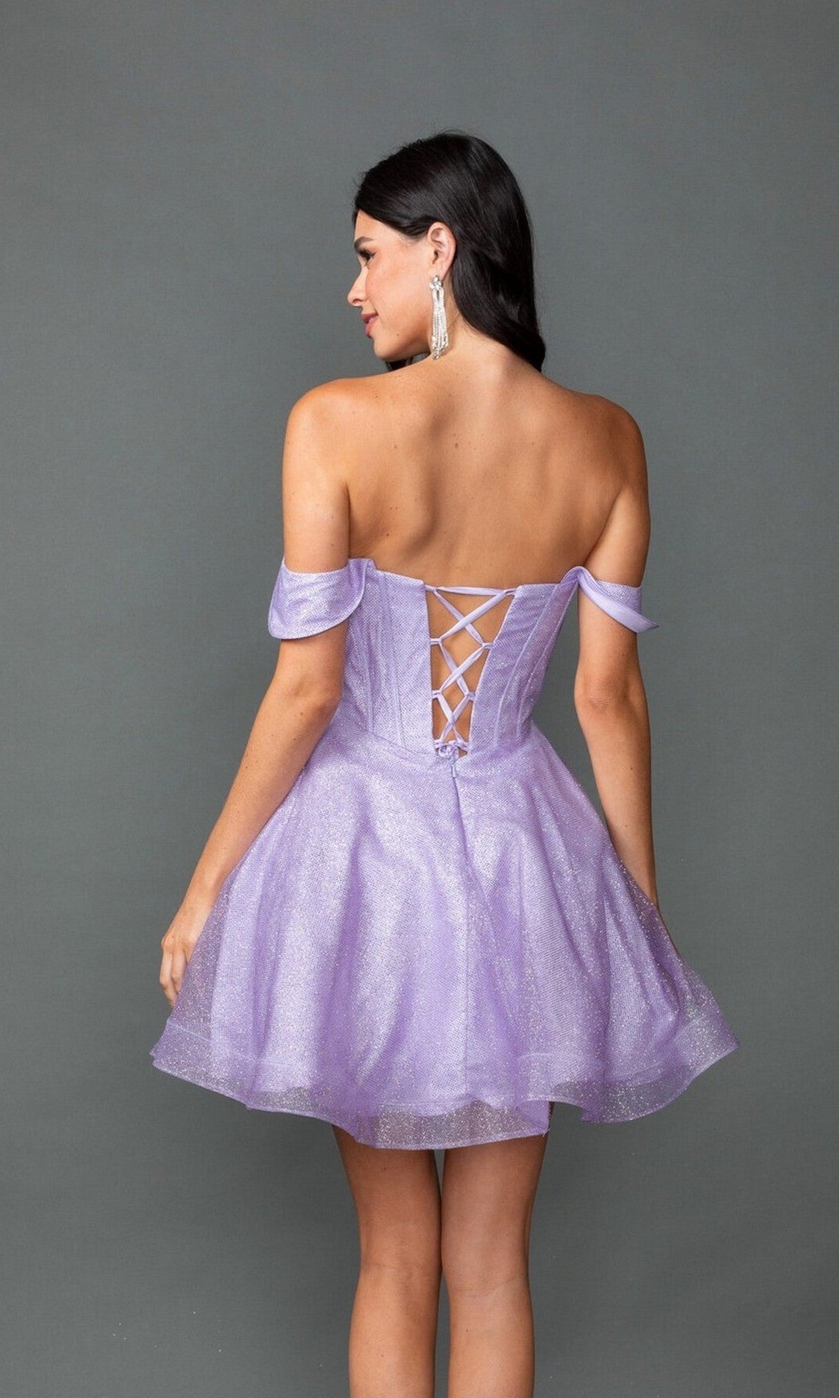 A woman models the Dancing Queen 3425 short prom dress in lavender, featuring an off-the-shoulder neckline, lace-up back, and fit-and-flare silhouette, set against a plain gray background.